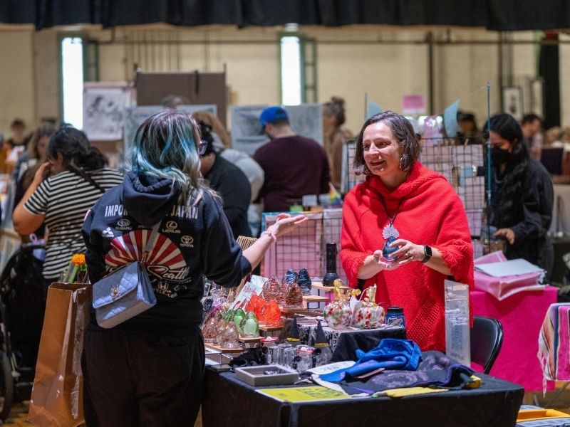 A vendor, Hidden Destiny Glass, talks about their artwork with a customer at Arts at the Armory. 