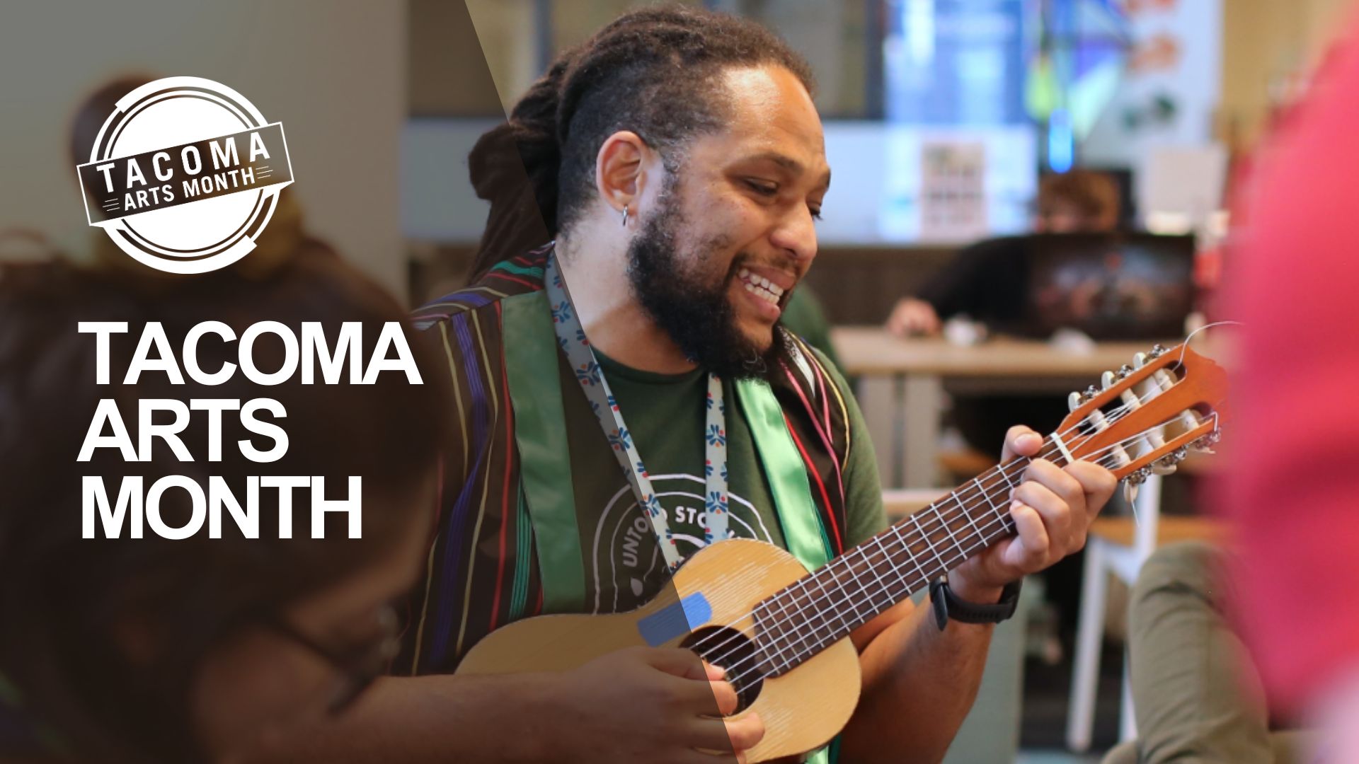 A person with dreadlocks is playing a ukulele and smiling. They are wearing a green shirt, a colorful striped vest, and red pants, as part of Kaleidoscope during Tacoma Arts Month.