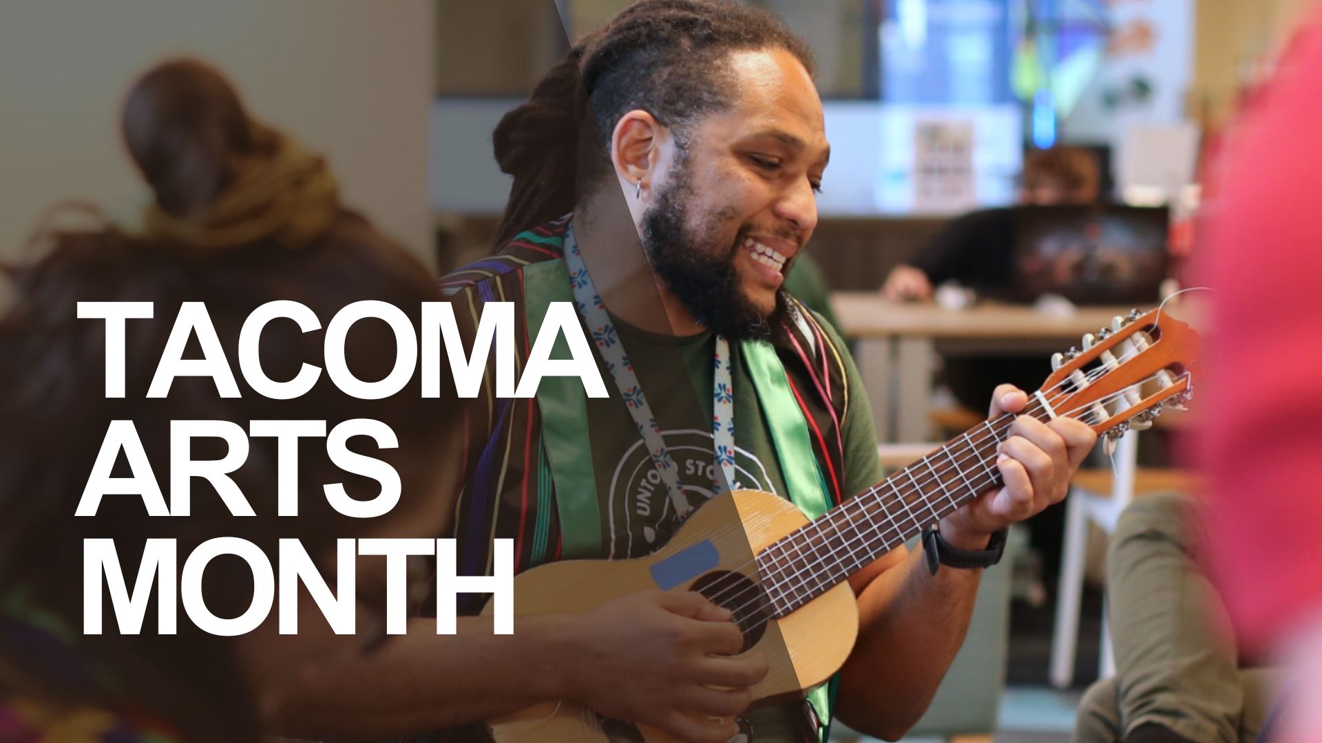 A person with dreadlocks is playing a ukulele and smiling. They are wearing a green shirt, a colorful striped vest, and red pants, as part of Kaleidoscope during Tacoma Arts Month.